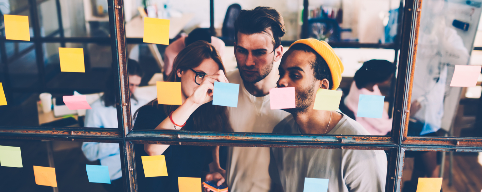 colleagues collaborating near transparent wall with stickers pondering on strategy